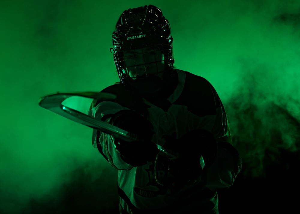 Keystone Kraken hockey player holding hockey stick in dramatic green lighting and fog during Media Day portrait session.