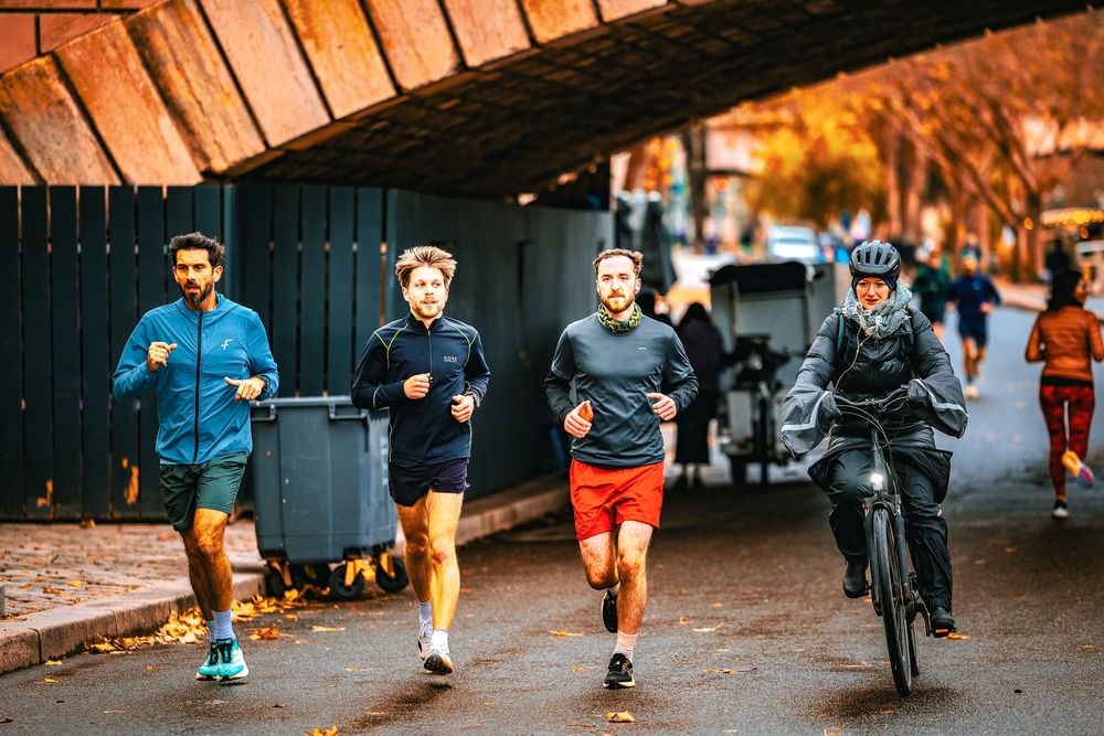 Group of runners and cyclist sharing a path under a bridge tunnel during an autumn morning workout session.
