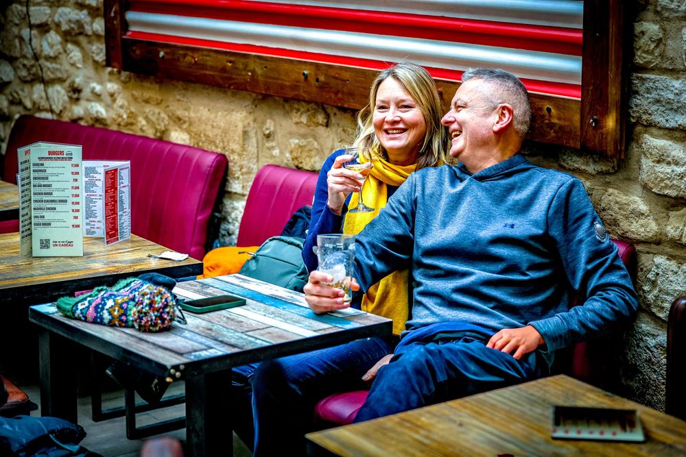 People sitting at outdoor tables at a restaurant or cafe with stone walls and colorful decor.