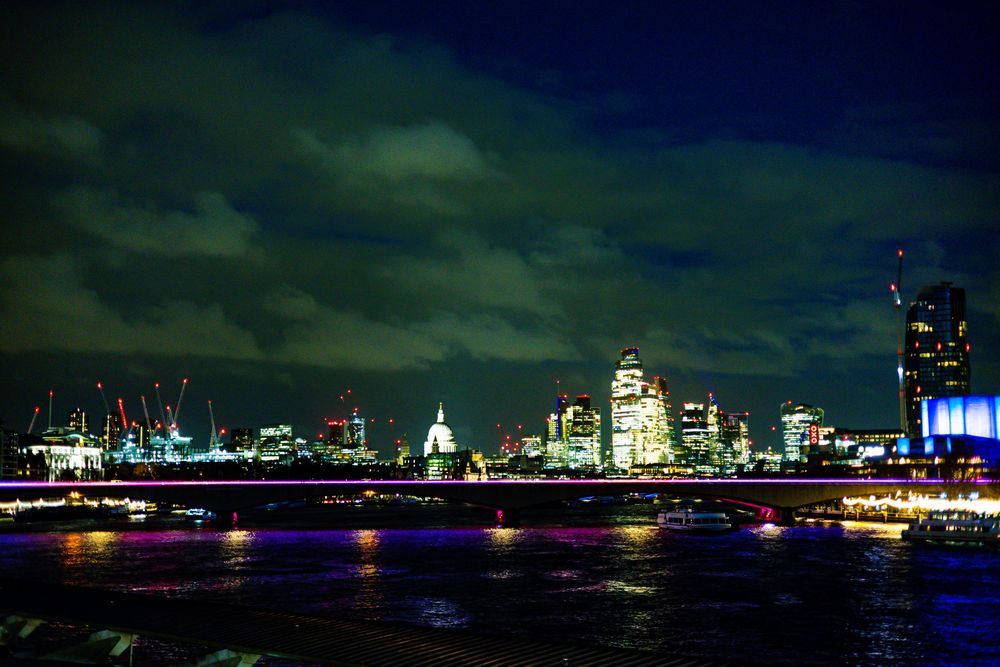 Panoramic cityscape skyline at night with illuminated buildings reflected on dark water.