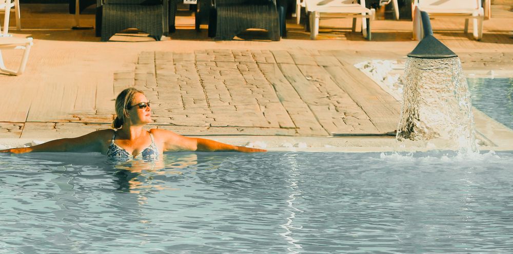 People enjoying a sunny day at a resort swimming pool with lounge chairs and umbrellas visible around the deck.