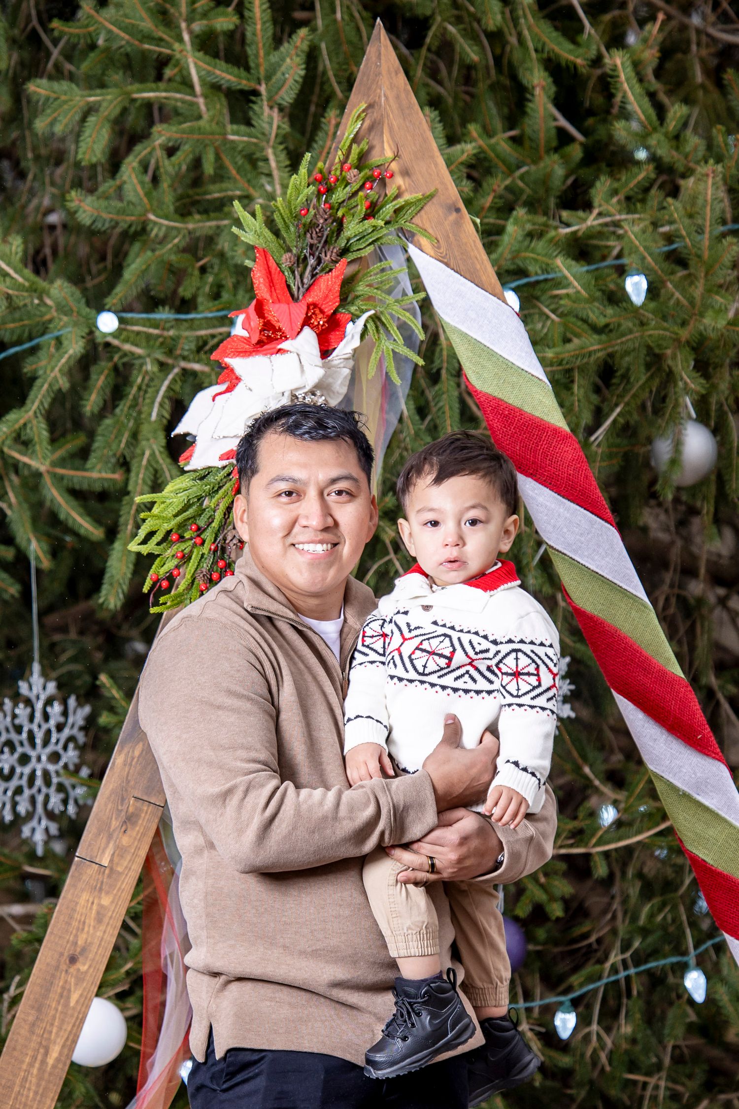 Holiday portrait session with matching Nordic sweaters against a decorated evergreen tree background.