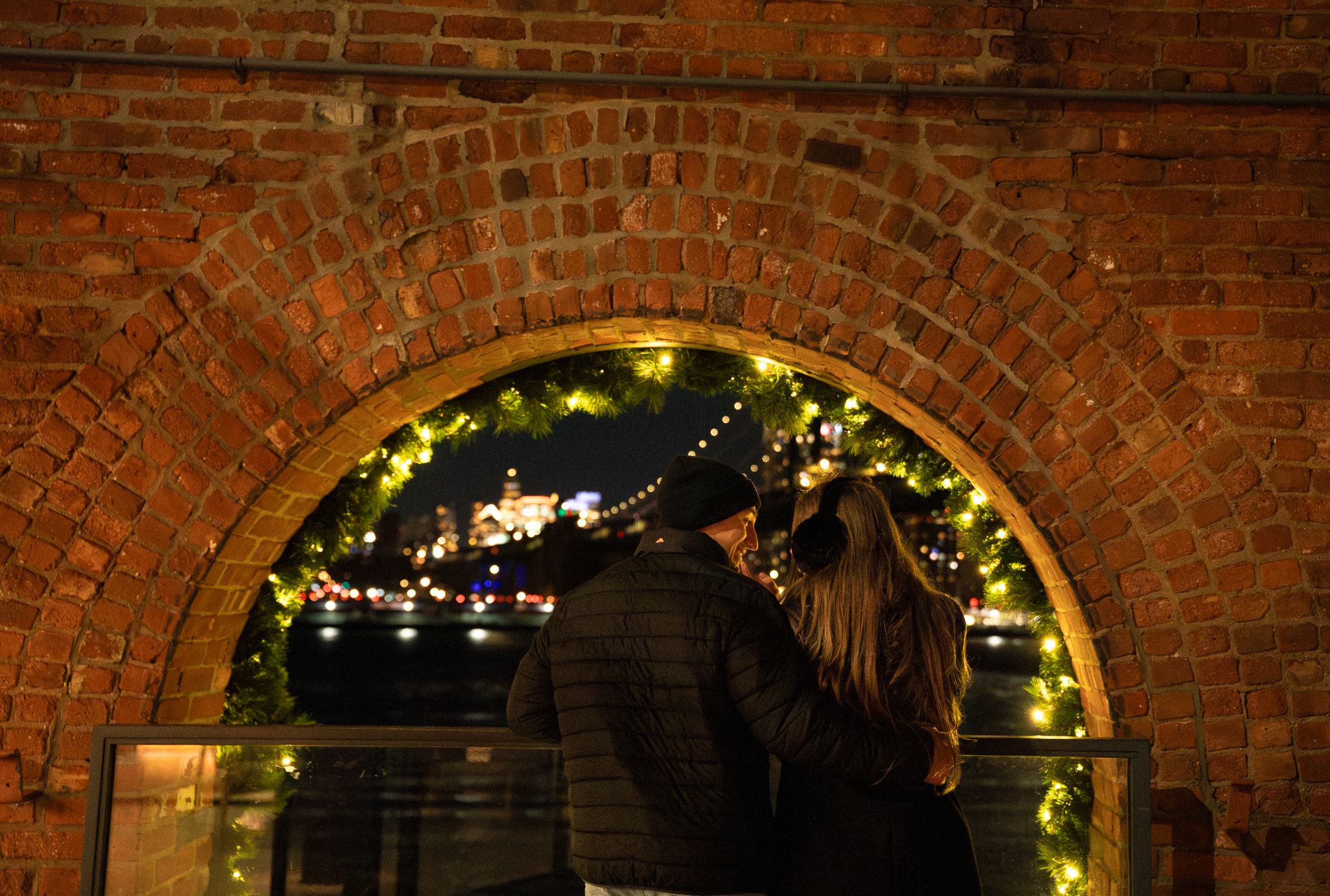 A romantic scene under a brick archway decorated with holiday lights.