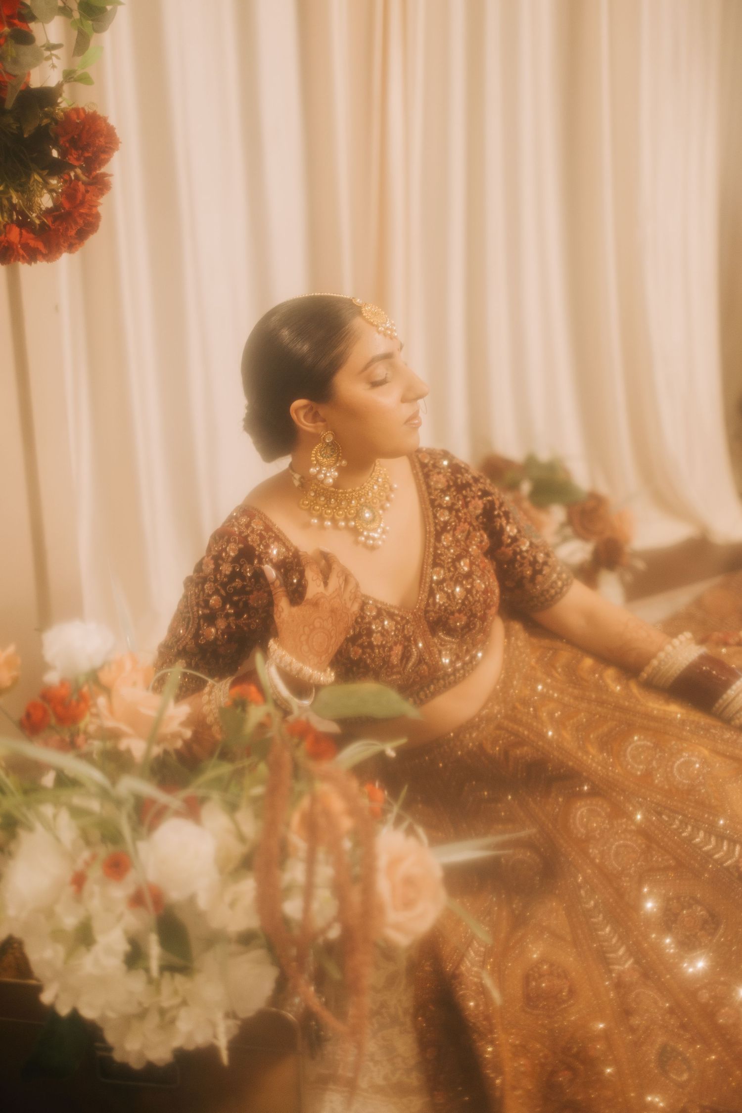 A romantic couple in traditional South Asian wedding attire share intimate moments in a garden setting with wooden lattice backdrop.