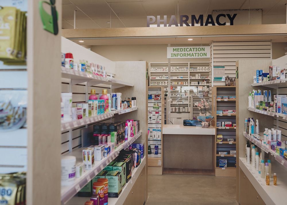 Interior view of a modern pharmacy with organized shelves of medications and healthcare products along the walls.