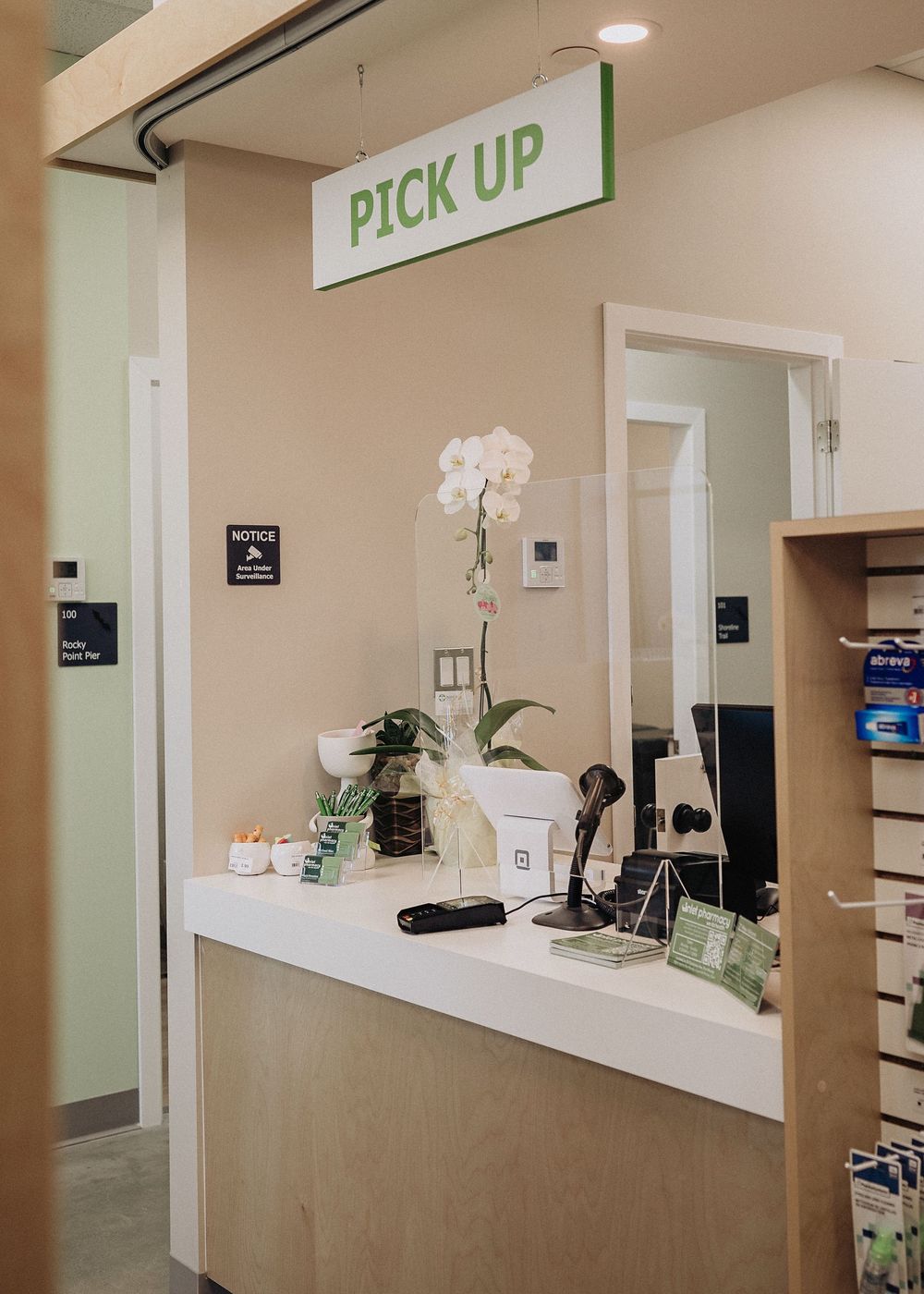 Modern dispensary interior with clean white pickup windows, wood accents, and decorative orchid plants on the counter.