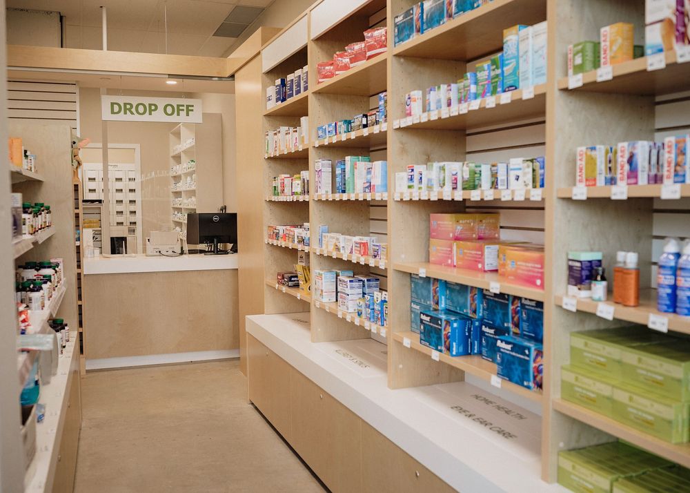 Wide angle view of a pharmacy interior with stocked shelves of medications and health products along beige walls.