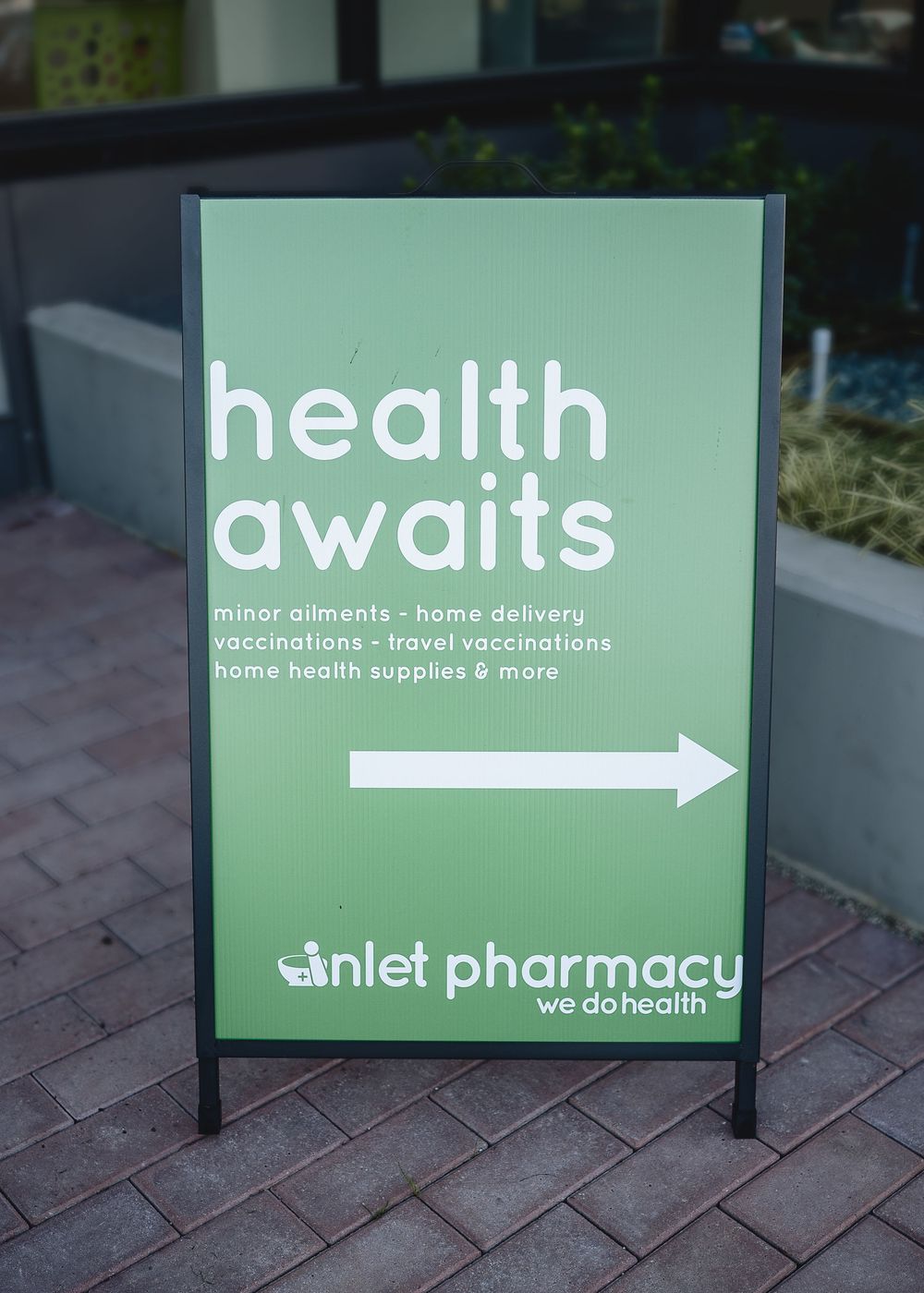 A series of green pharmacy signs displaying 'health awaits' with directional arrows for home delivery and consultation services.