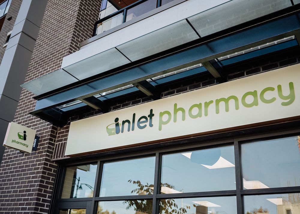 Modern storefront exterior of Inlet Pharmacy with white signage mounted on dark brick building under glass awning.