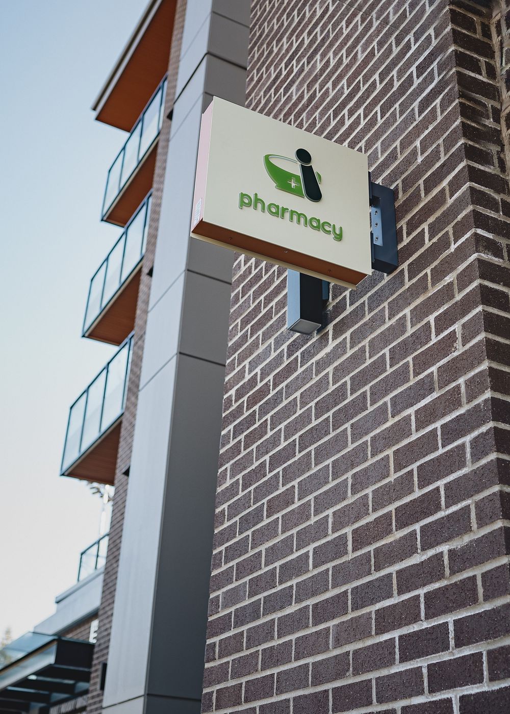 Modern brick building facade with a pharmacy sign and glass windows against an overcast sky.