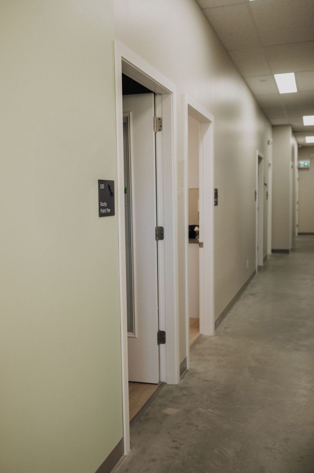 Long institutional hallway with white walls, fluorescent lighting, and multiple closed doors along both sides.