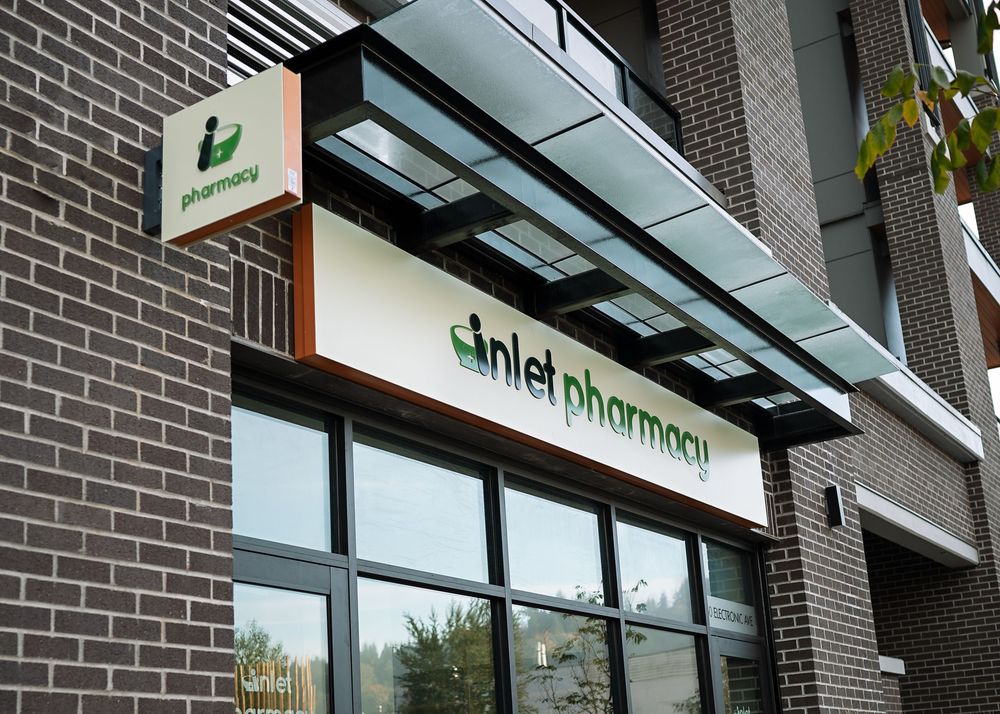 Modern brick building exterior with illuminated pharmacy signage and storefront windows at dusk.