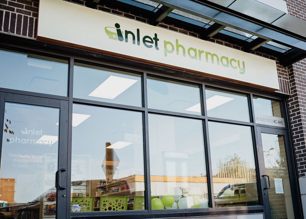 Modern pharmacy storefront with large glass windows and illuminated signage displays the name 'Inlet Pharmacy' on exterior.
