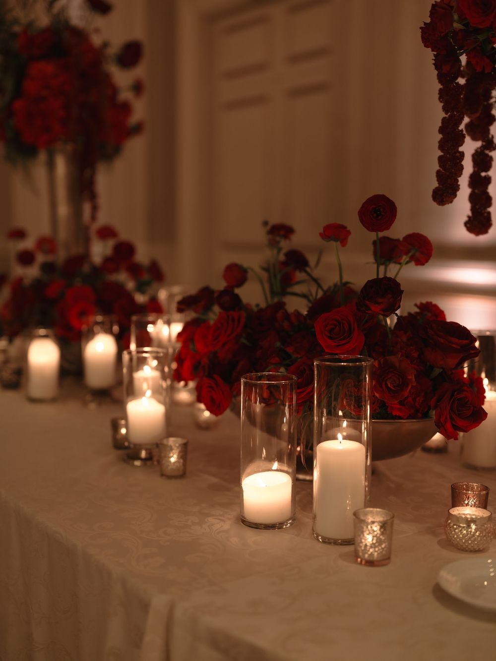 Elegant wedding reception table decorated with glowing candles and deep red floral arrangements creating a romantic ambiance.