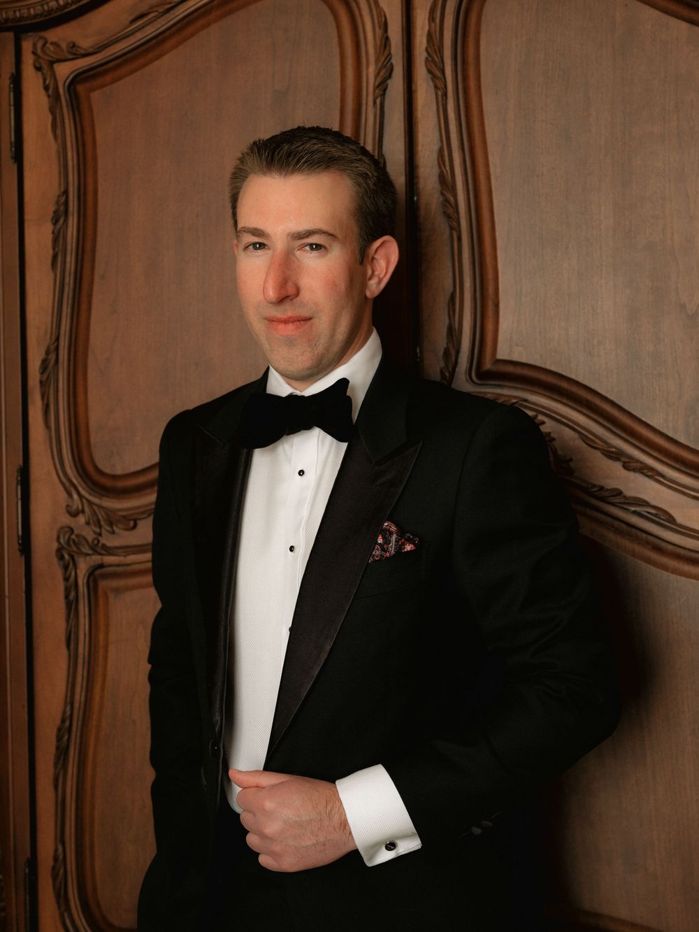 A person in formal black tuxedo and white shirt poses against an ornate brown wall in a series of elegant portraits.
