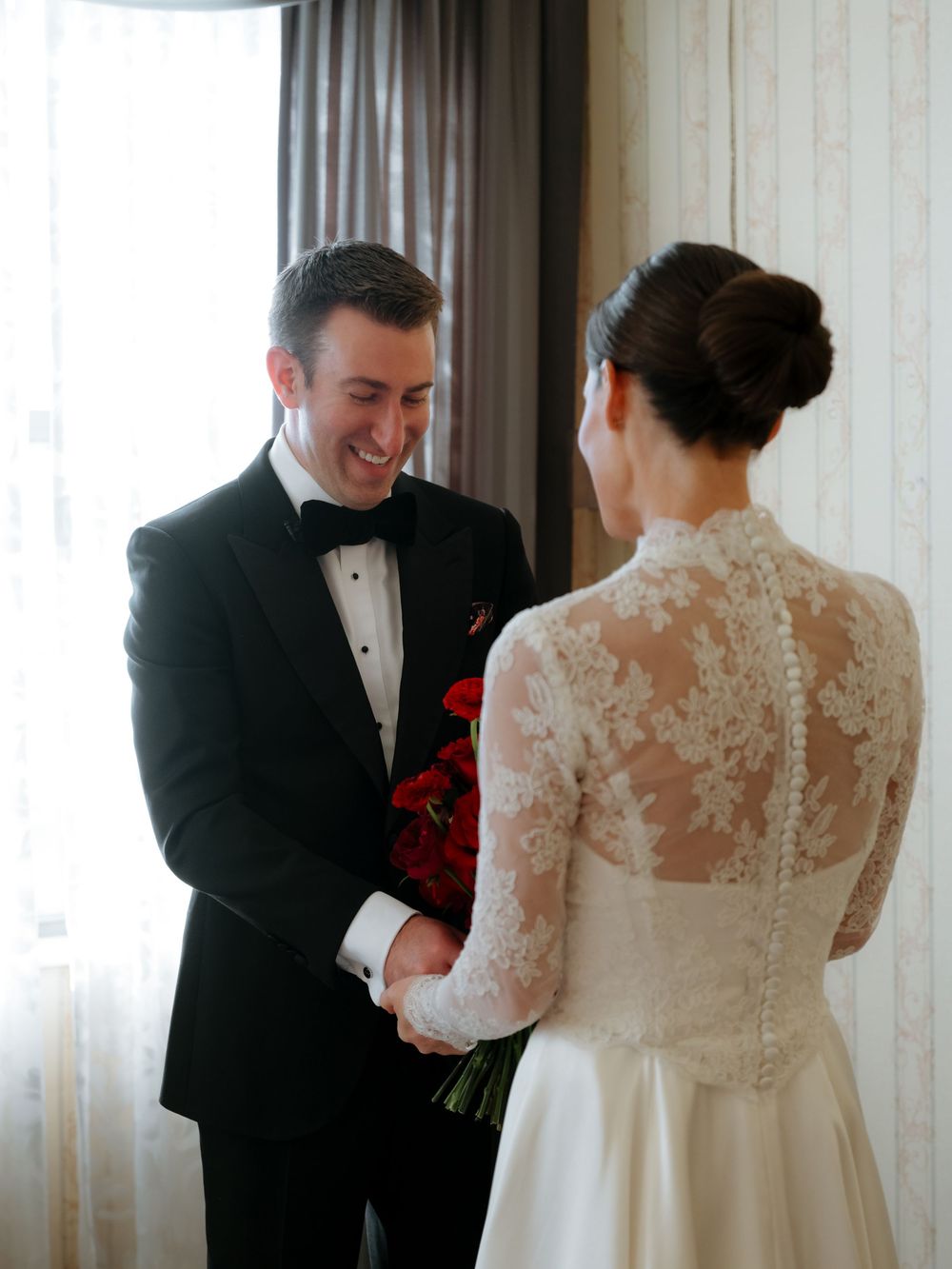 First look moment between bride in lace back dress and groom in tuxedo during wedding day.