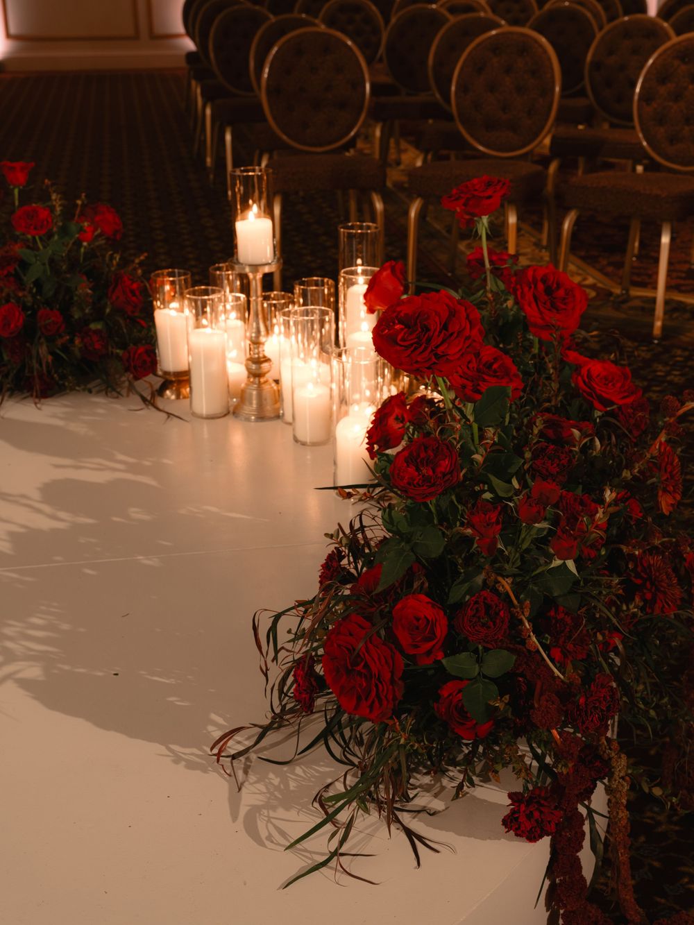 Elegant table setting with glowing white candles and dramatic red roses creating a romantic ambiance.