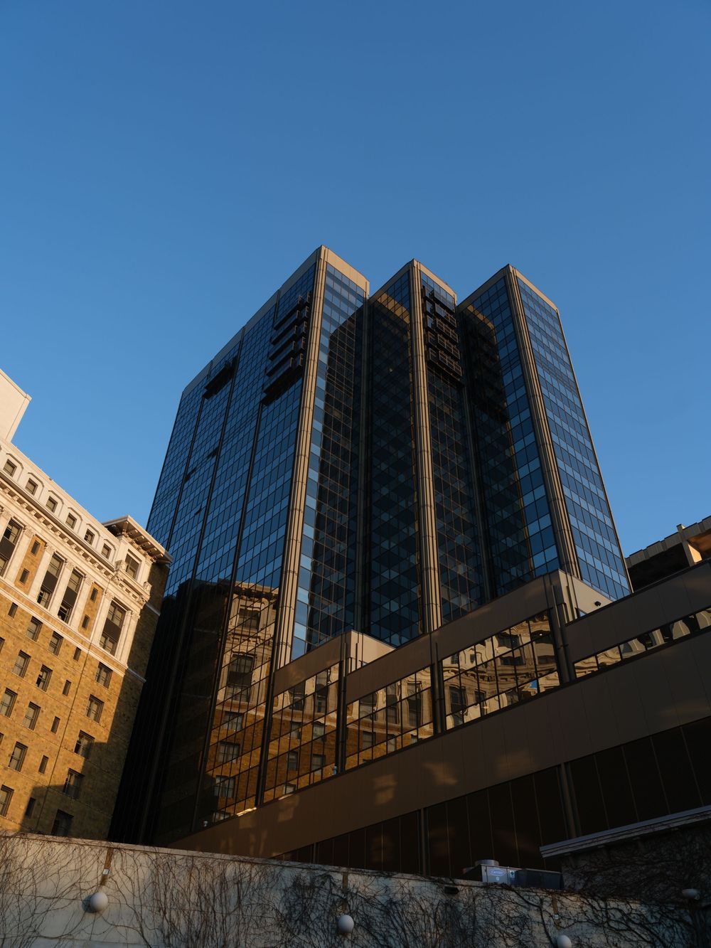 Modern glass office building facade with reflective windows against blue sky creates geometric patterns and shadows.