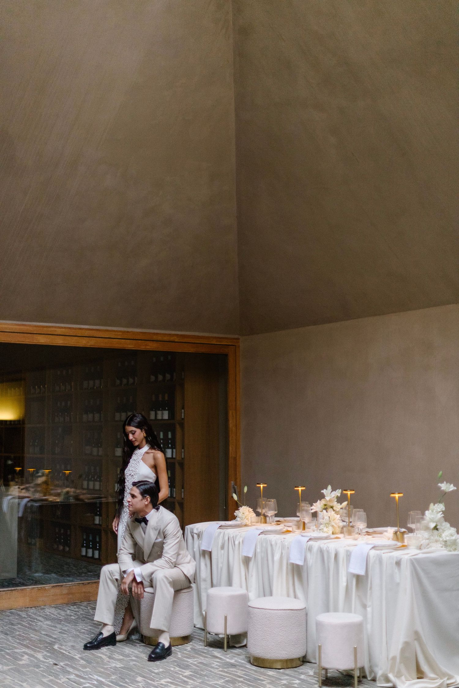 Elegant wedding reception setup with white tablescapes and decorative details next to a modern interior window display.