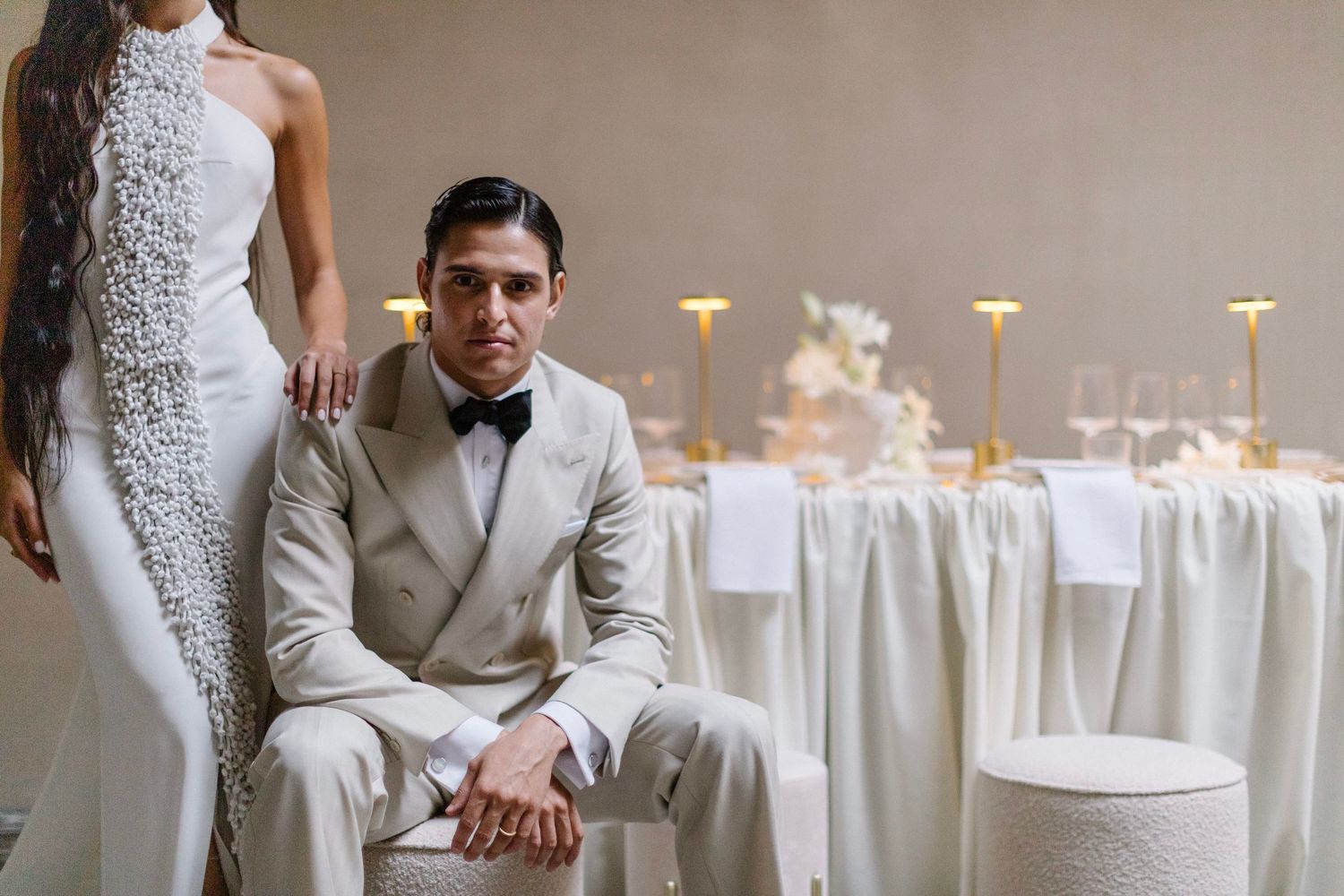 Elegant wedding reception setup with white tables and tall candles in a neutral-toned venue.