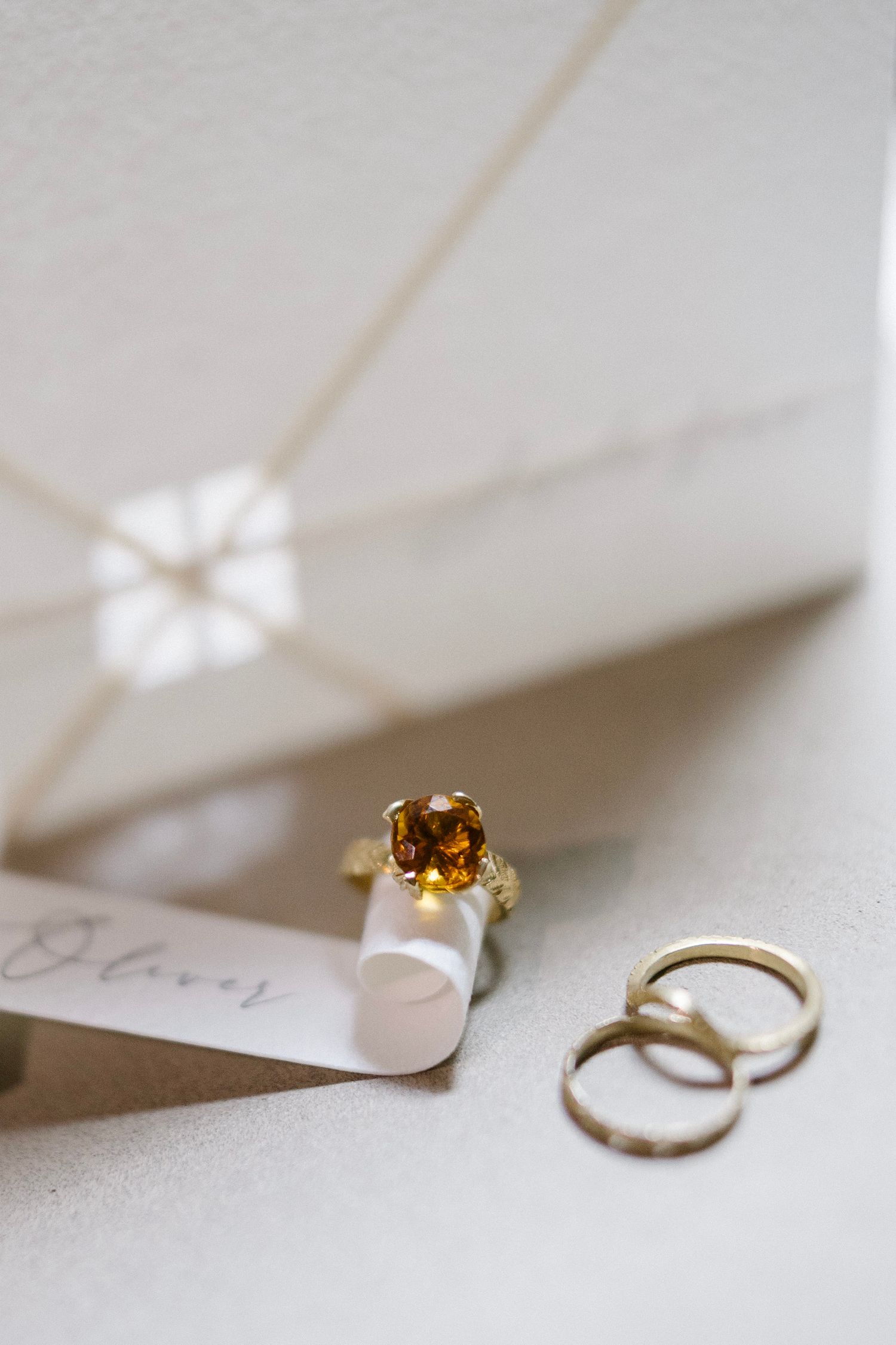 Gold engagement ring with amber gemstone and two wedding bands displayed on white paper with soft lighting.