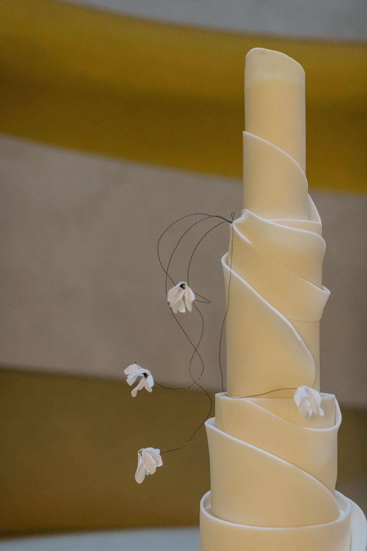Modern white wedding cake with delicate spiral design and small floral accents.