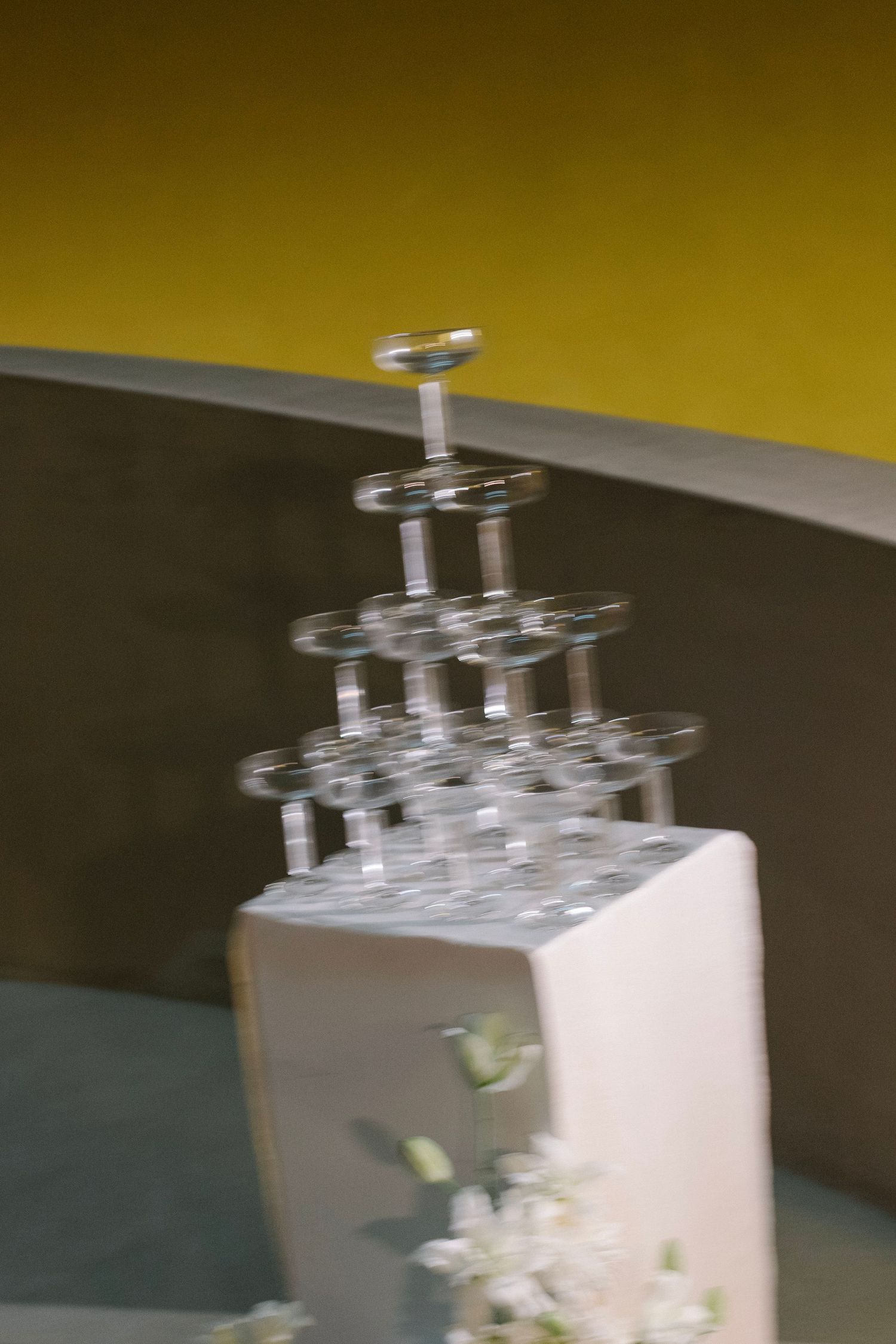 Sequence showing champagne glasses being stacked into a pyramid formation against yellow background.