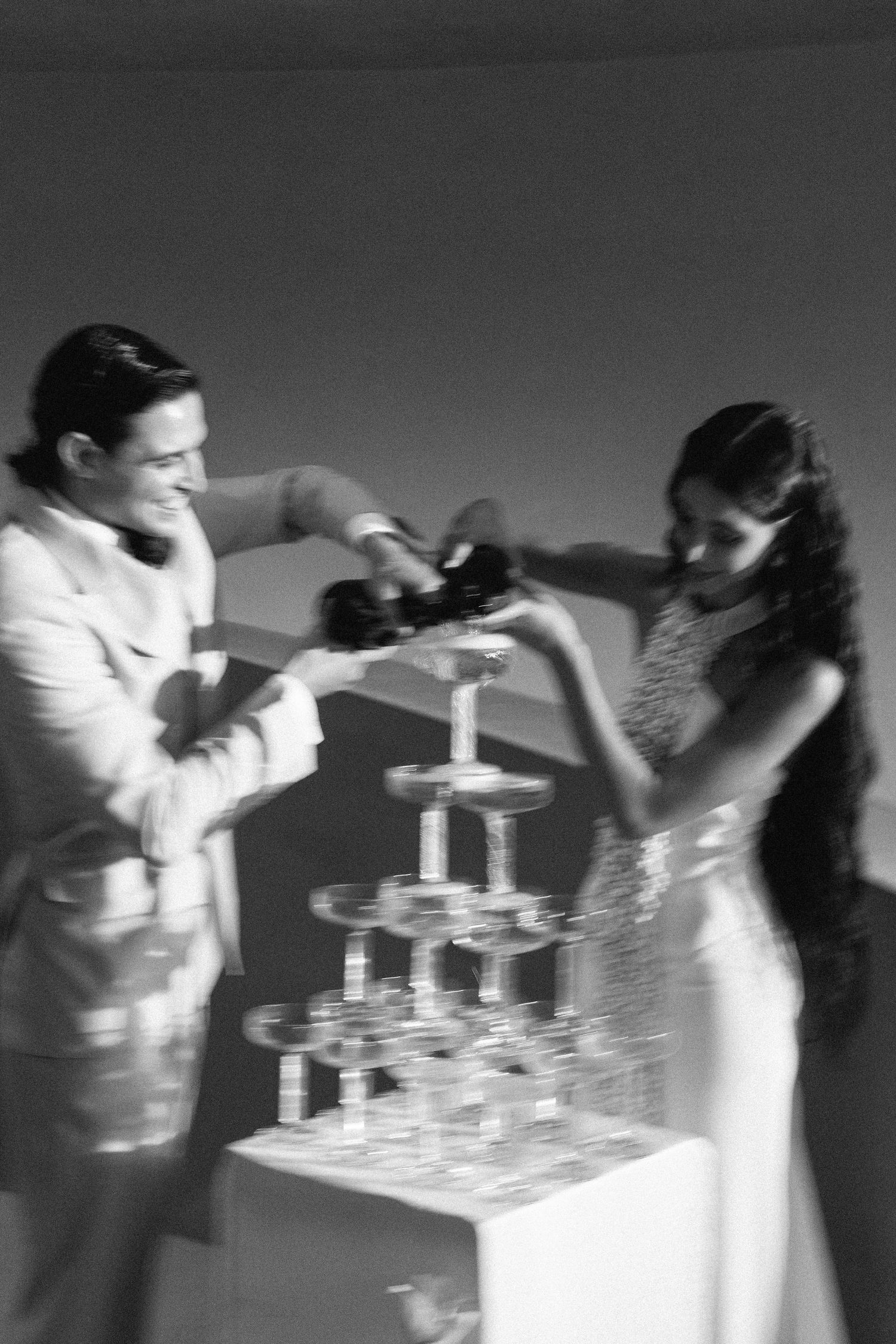 Couple pouring champagne into a tower of glasses at their wedding celebration.