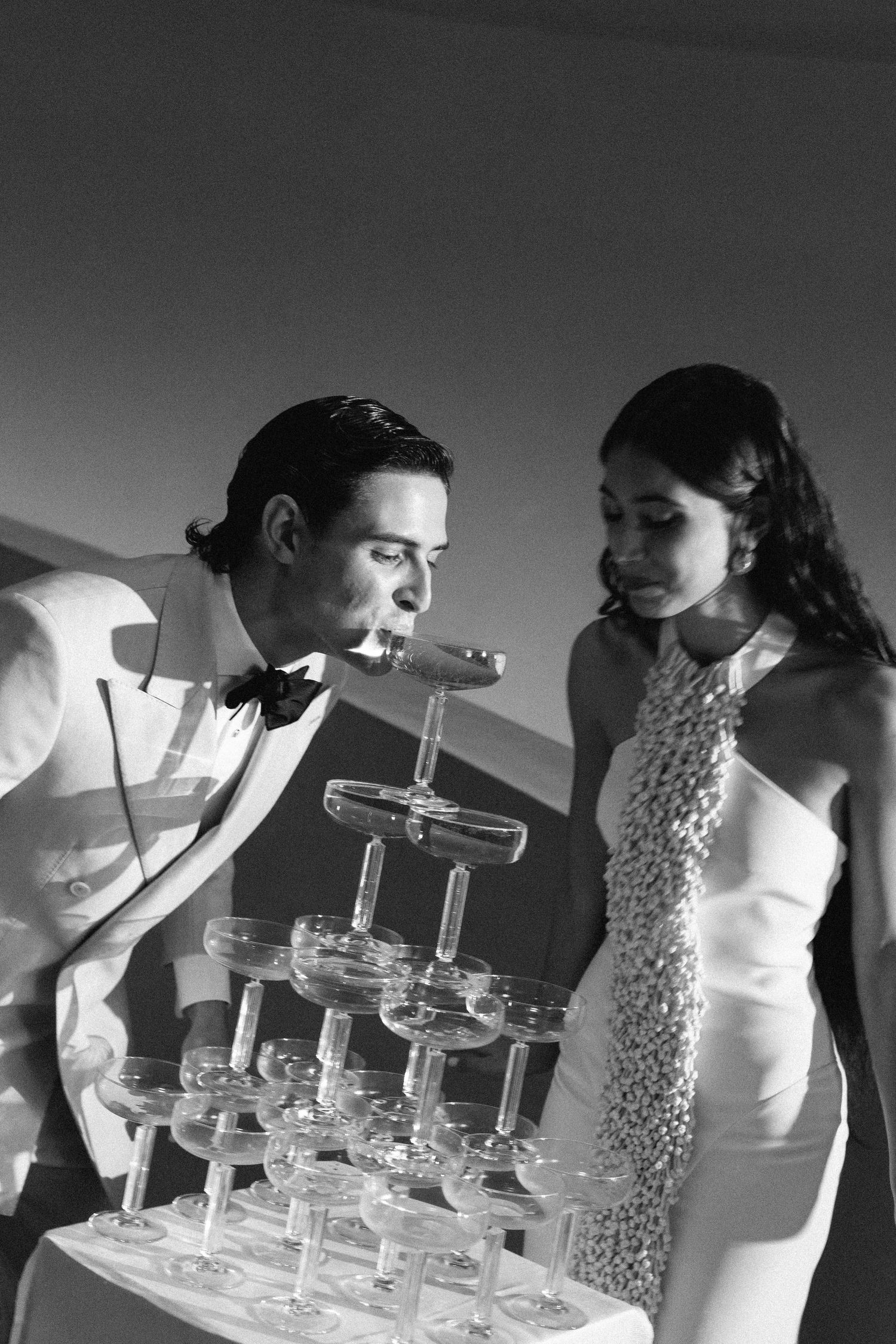 Black and white photo sequence showing someone leaning over a tiered display of champagne glasses.
