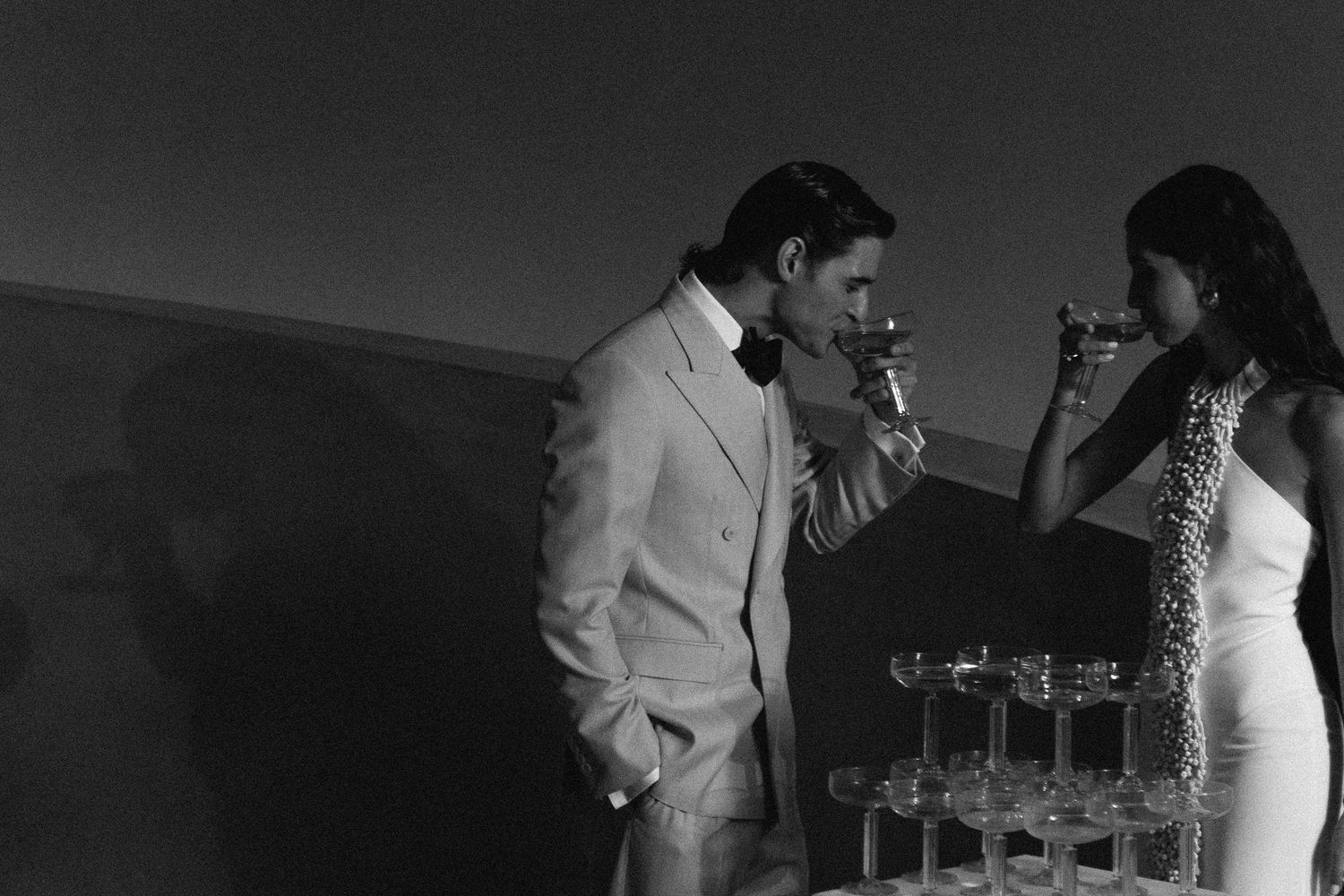 Wedding reception guests mingling and holding champagne glasses in dark lighting.