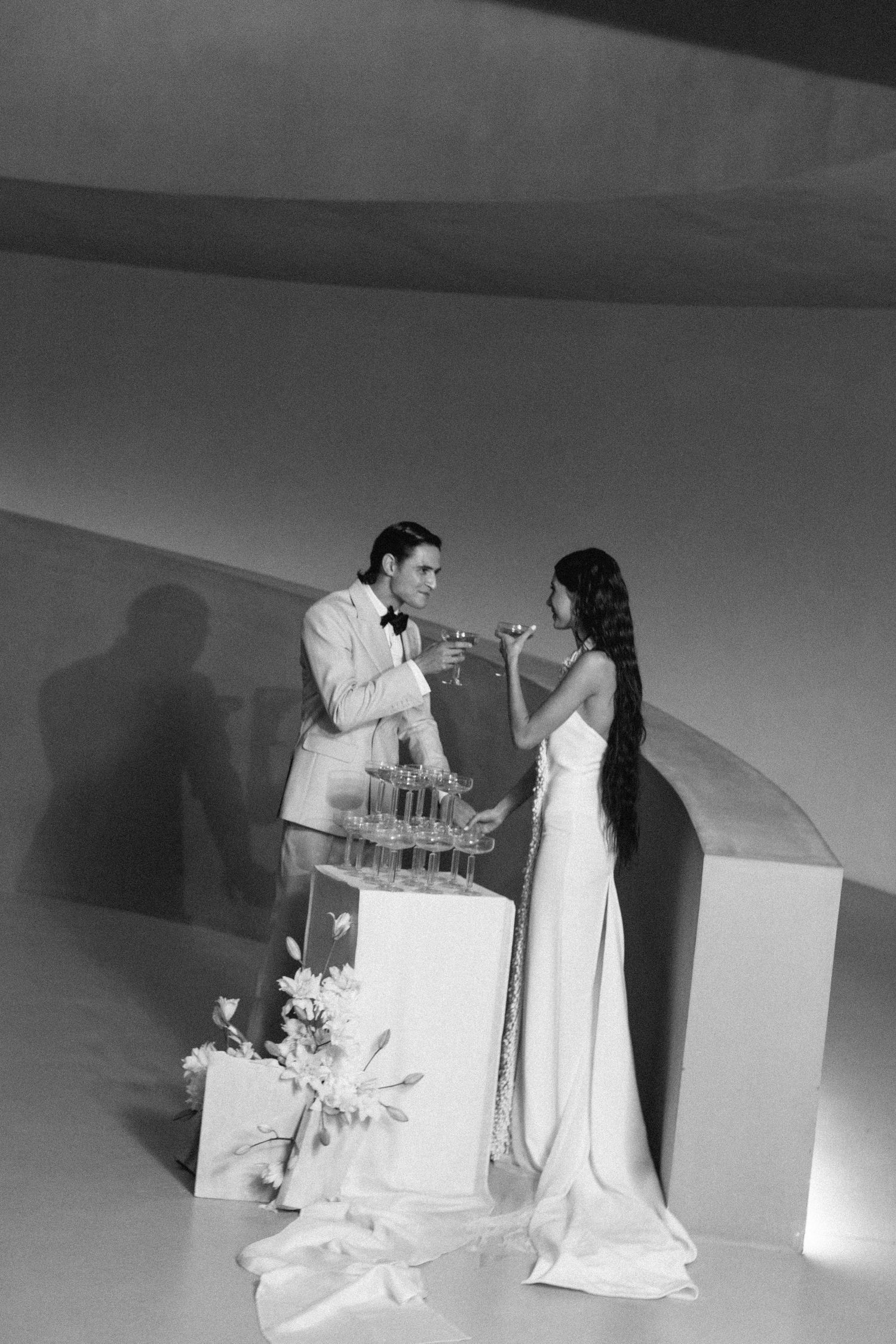 Wedding couple sharing champagne together next to their tiered white cake in black and white photography.
