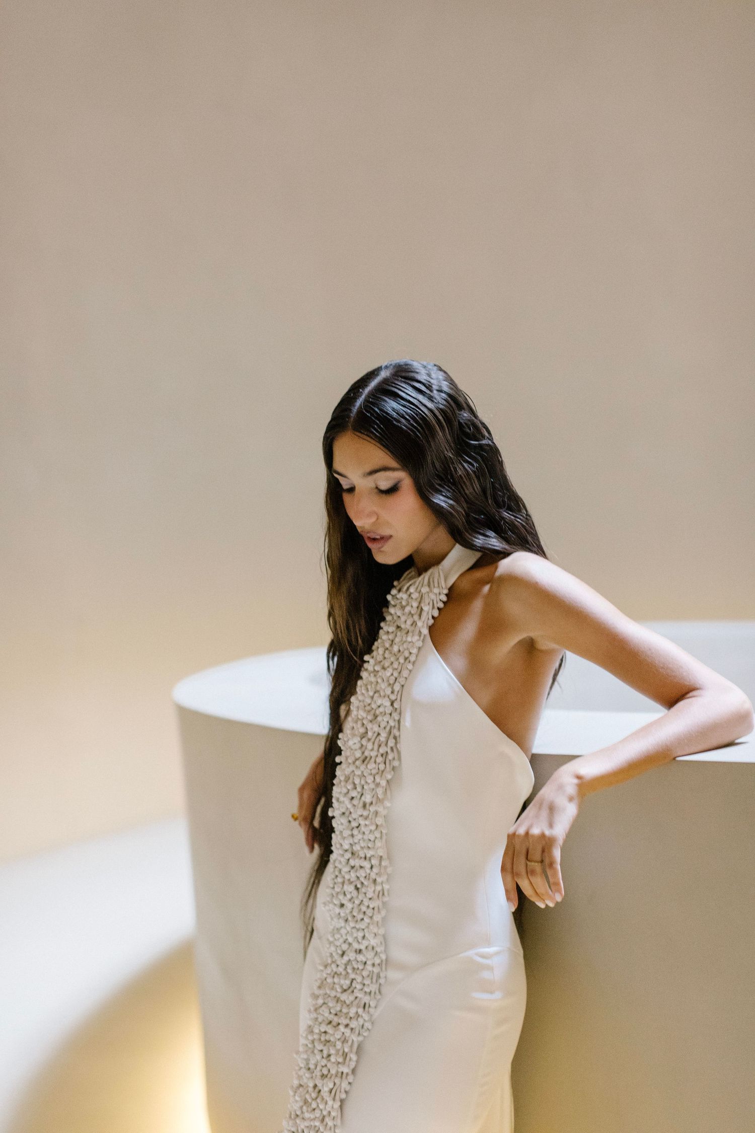 Bride in an elegant halter neck lace wedding dress poses against a minimalist curved wall.