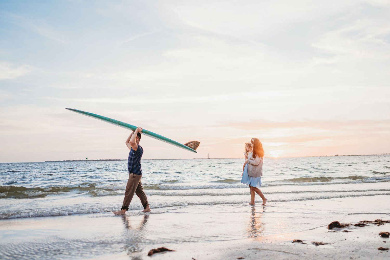 Two people carrying surfboards walk along a beach at sunset with waves crashing on the shore.