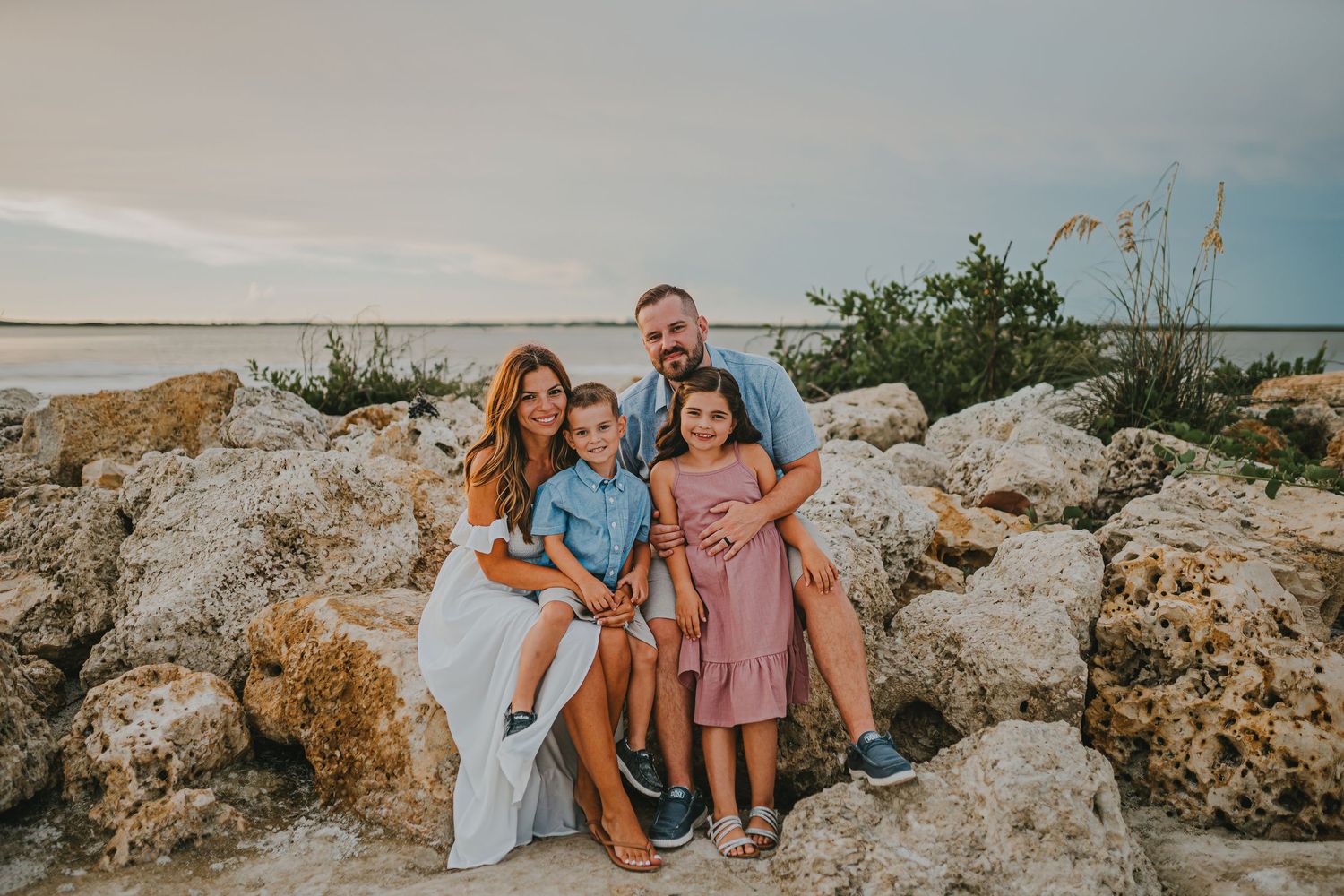 Family sitting together on coastal rocks during sunset at a beach while enjoying the ocean view.