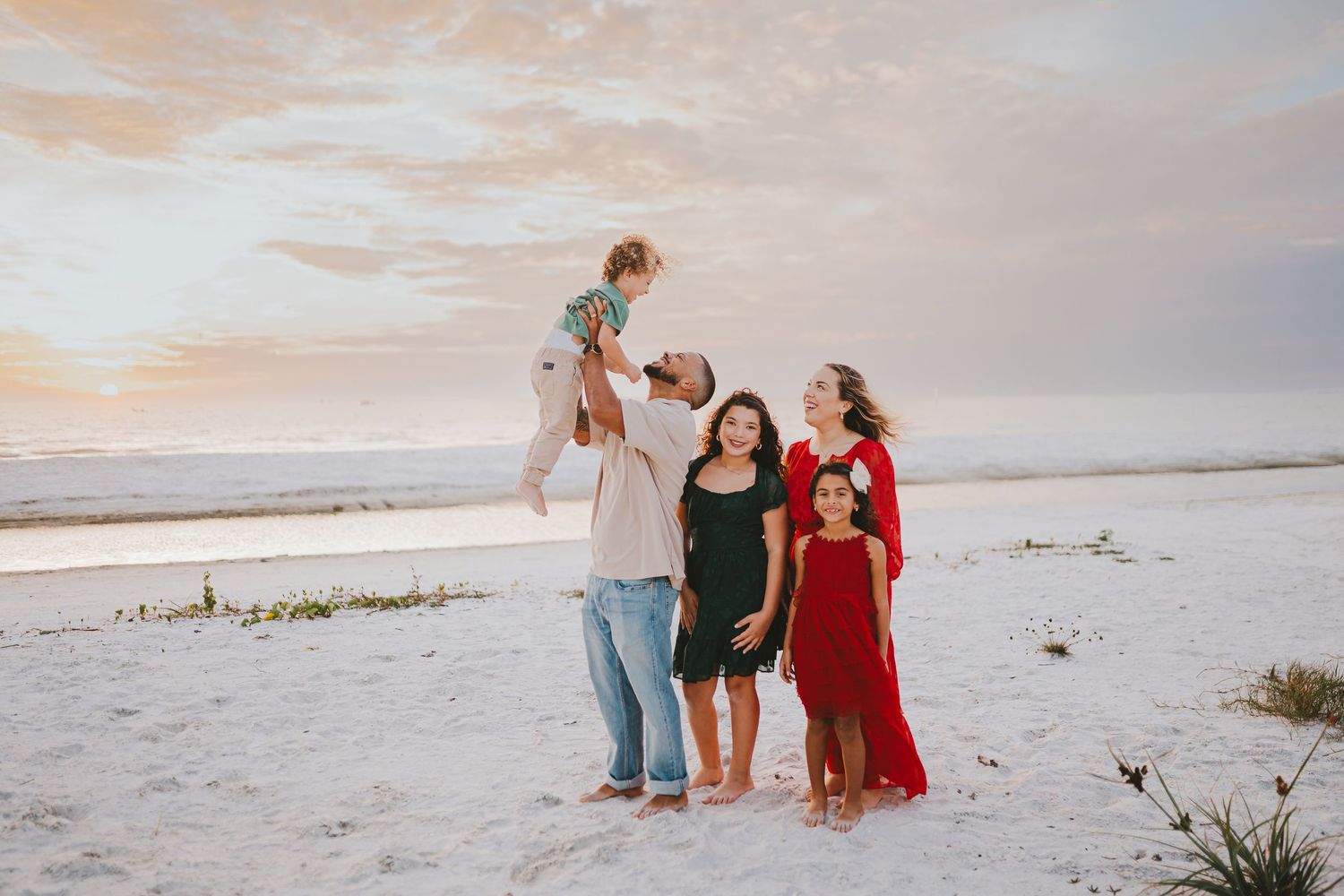 A family in coordinating outfits walks along a white sandy beach during sunset, creating silhouettes against the sky.