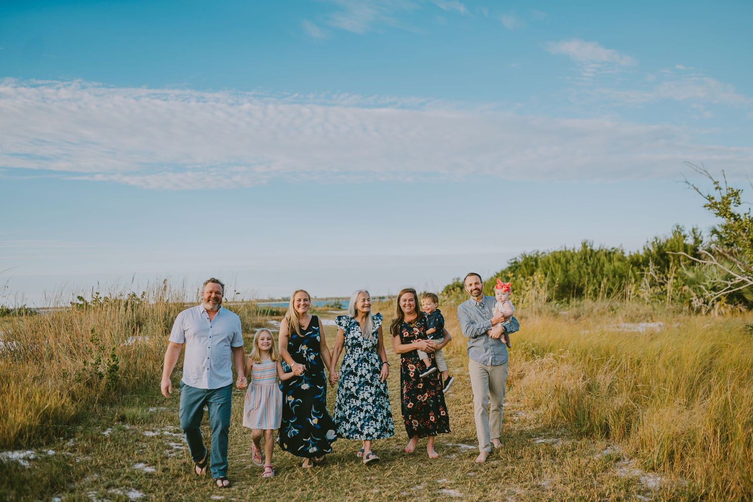 A group of people walking through tall golden grass along a coastal path on a bright sunny day.