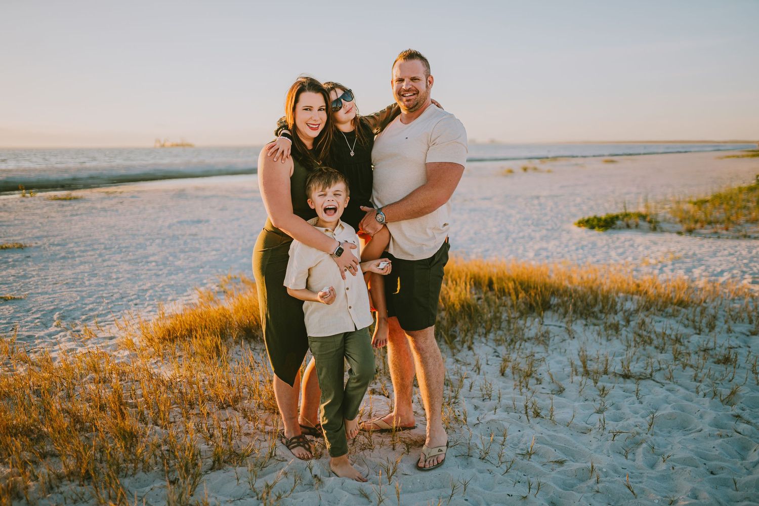 A family stands together on a sandy beach at sunset with golden light illuminating the coastal landscape.