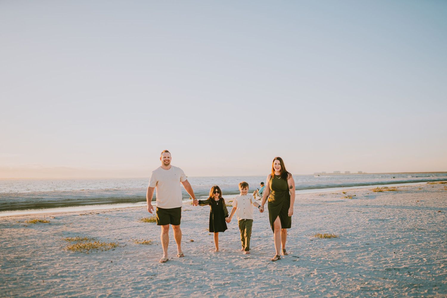 People walking along a sandy beach at sunset with mountains visible in the distance.