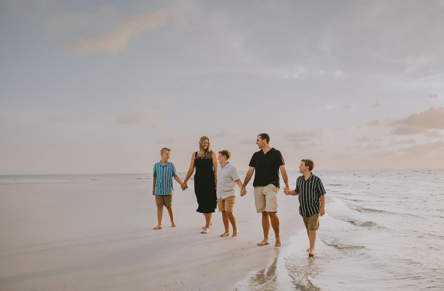 A group walks along a serene beach at sunset, their silhouettes casting long shadows on the wet sand.
