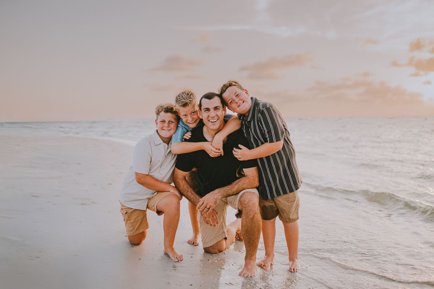 Family walking and playing together along a sandy beach at sunset with ocean waves in the background.