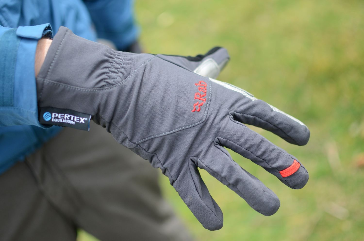 Close-up of gray Gore-Tex climbing gloves with red accents shown in detail against green background.