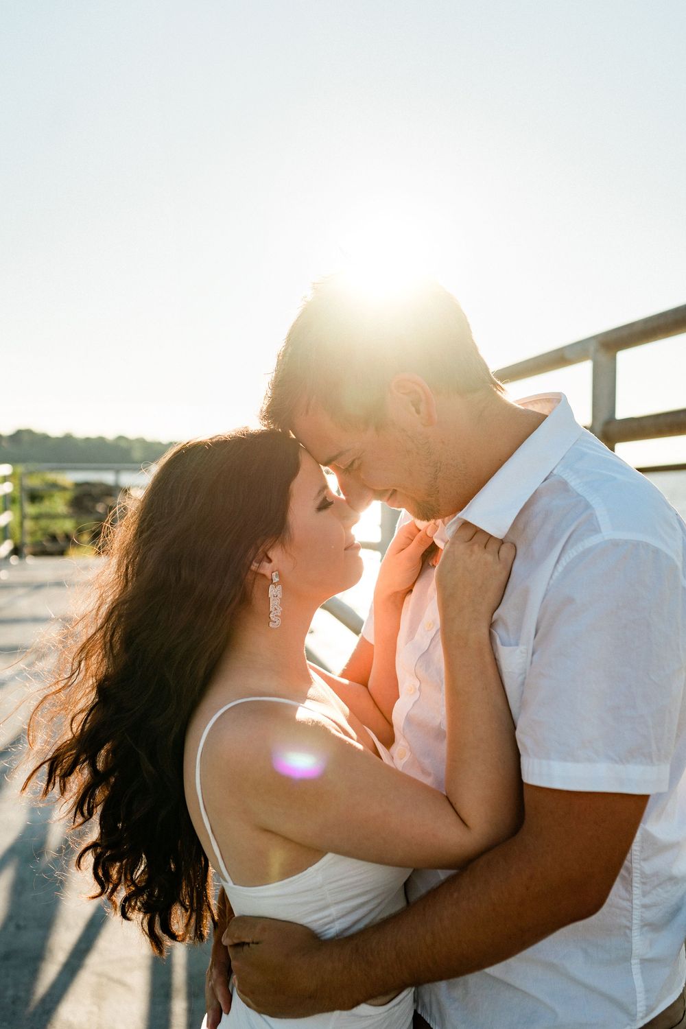 Romantic couple embracing and kissing on a beach at sunset with golden light filtering through their silhouettes.