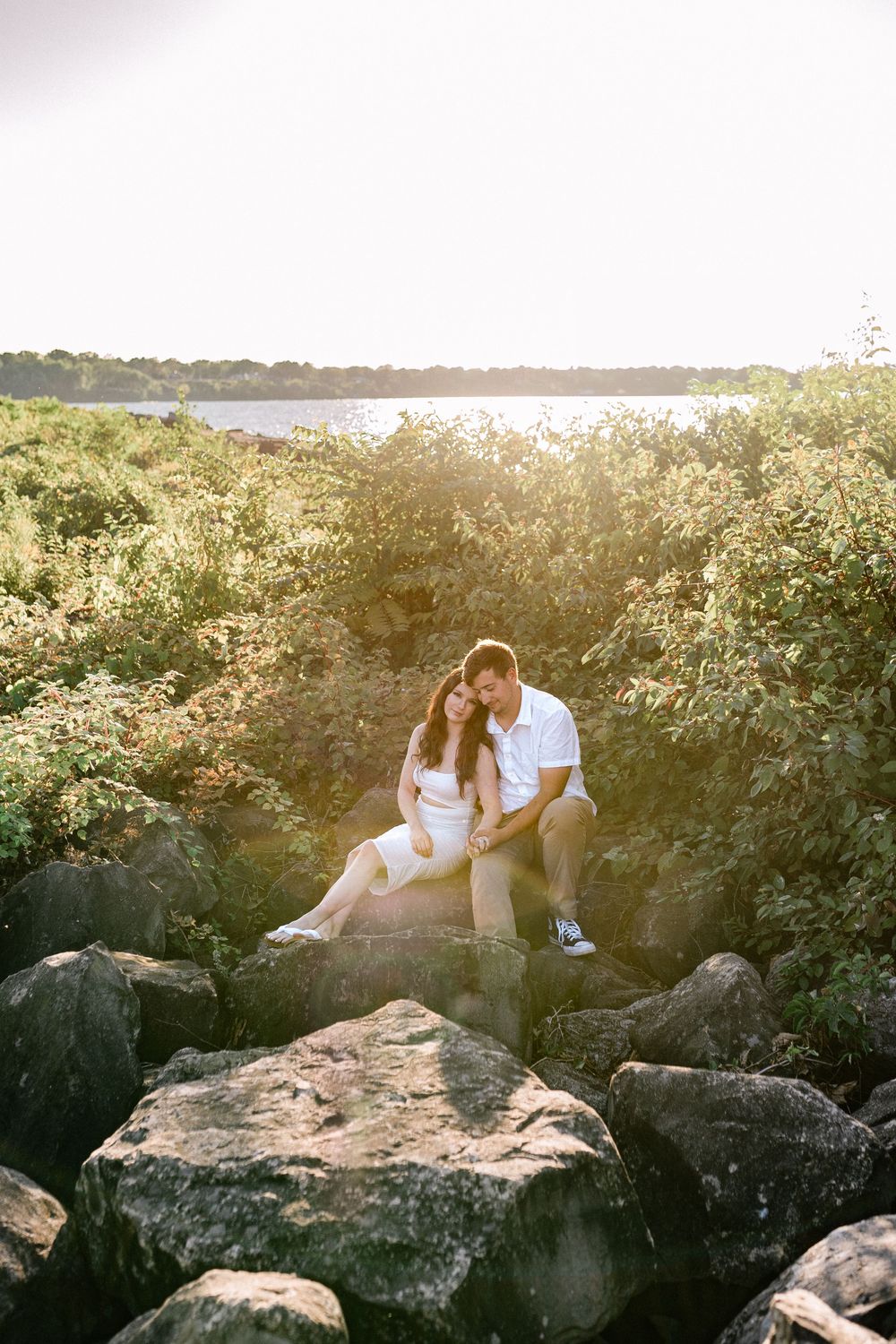 Romantic couple sitting on coastal rocks during golden hour by the water.