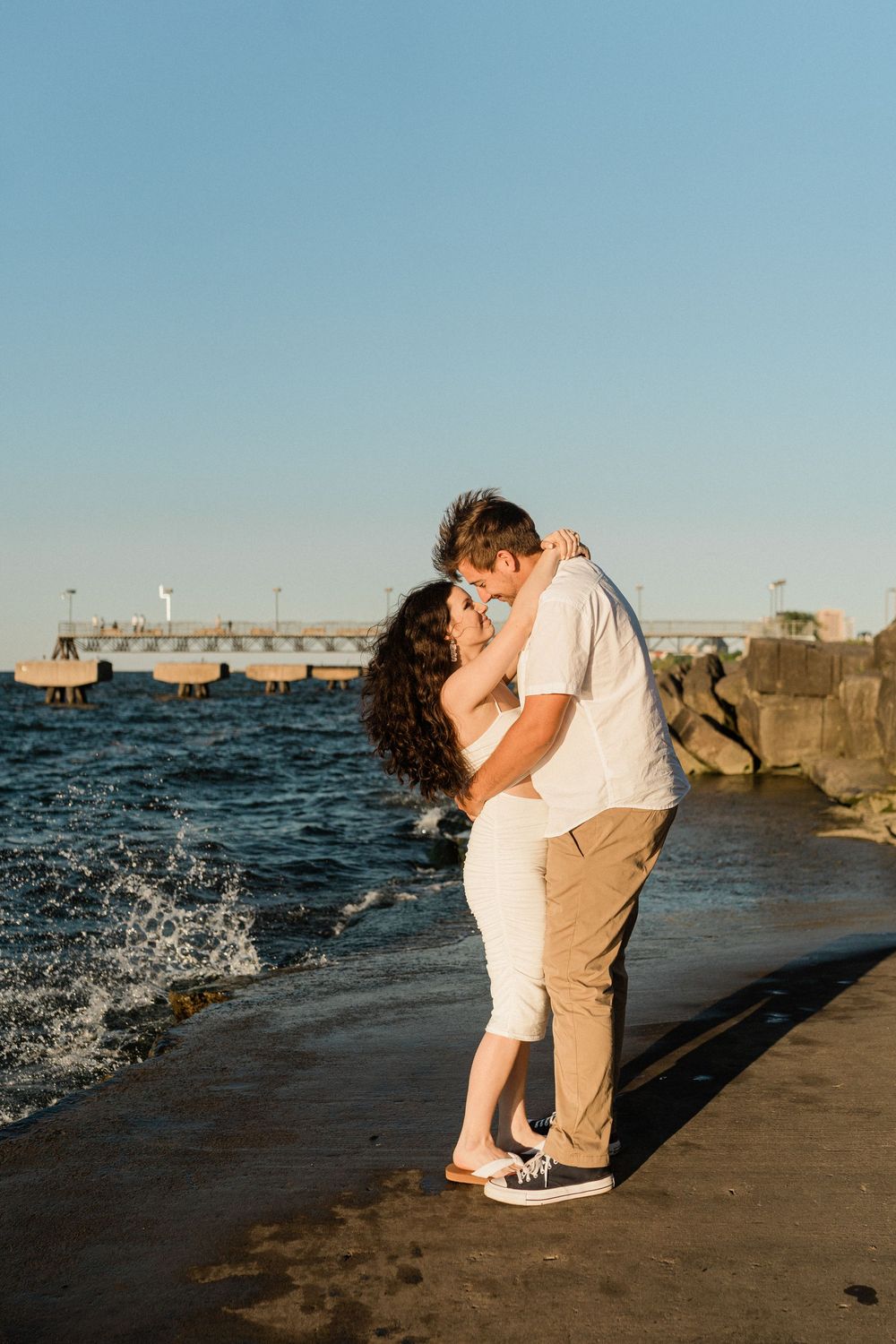 Romantic couple sharing an intimate moment on a rocky pier with waves crashing nearby.