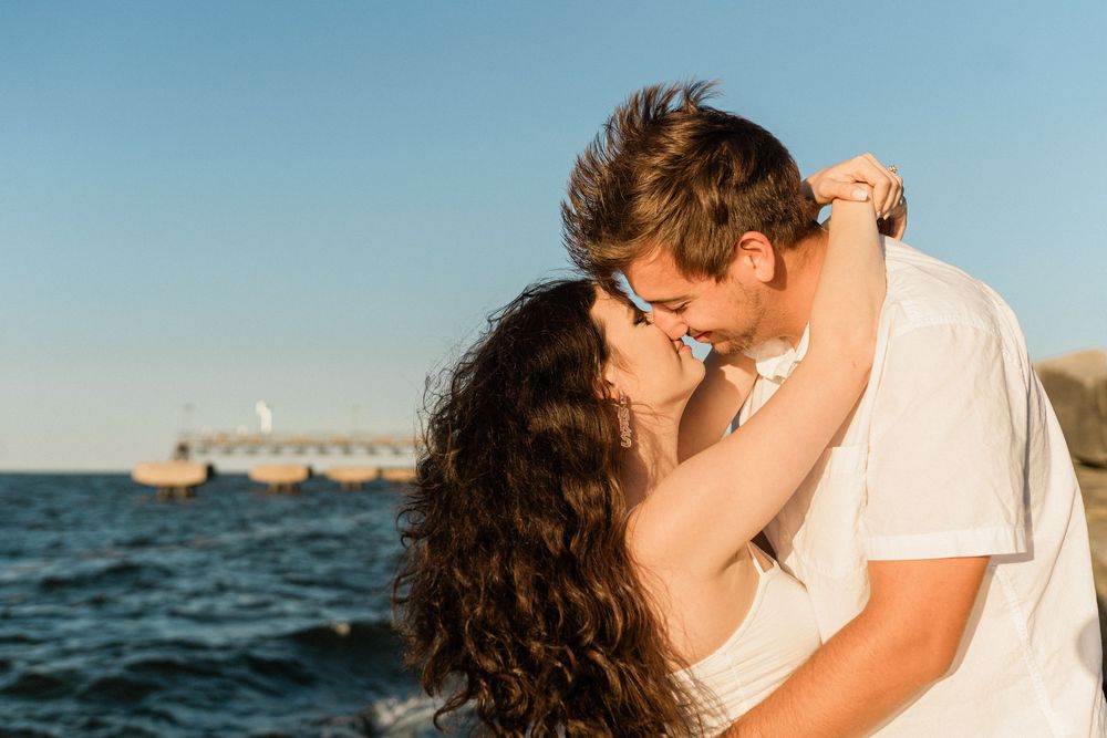Loving couple shares intimate moments against a scenic ocean backdrop during sunset.