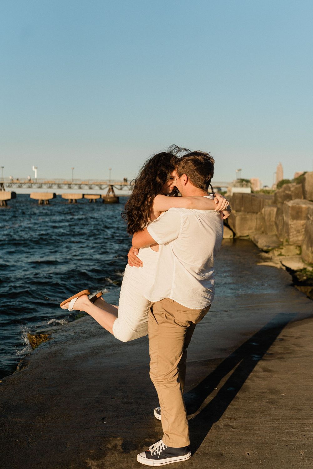 Romantic couple embracing at sunset on a stone pier by the ocean.