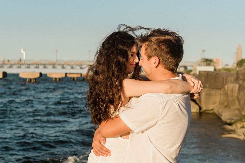 A romantic couple shares tender moments along a seaside pier with waves and ocean in the background.