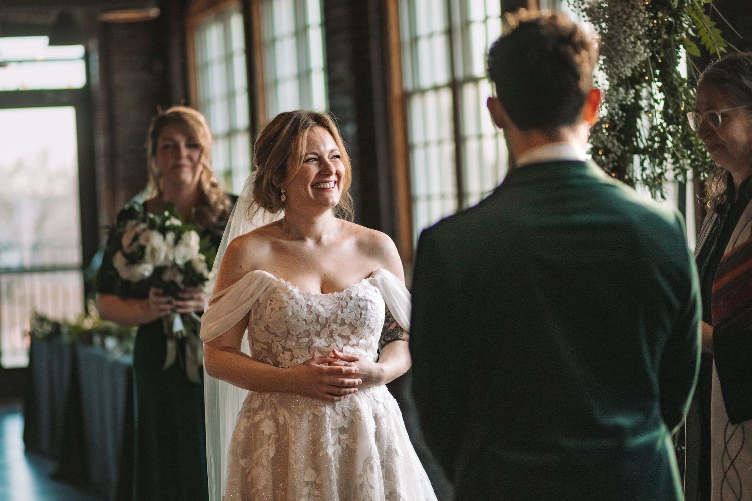 A wedding couple embraces during their first dance in a rustic industrial venue with warm lighting and greenery.