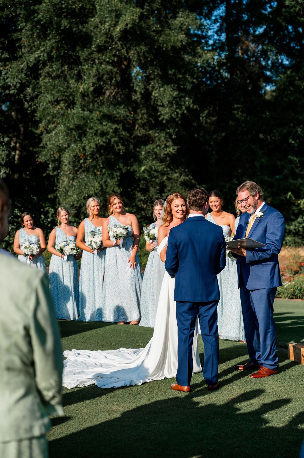 Wedding party gathers on golf course with bridesmaids in pale blue dresses.