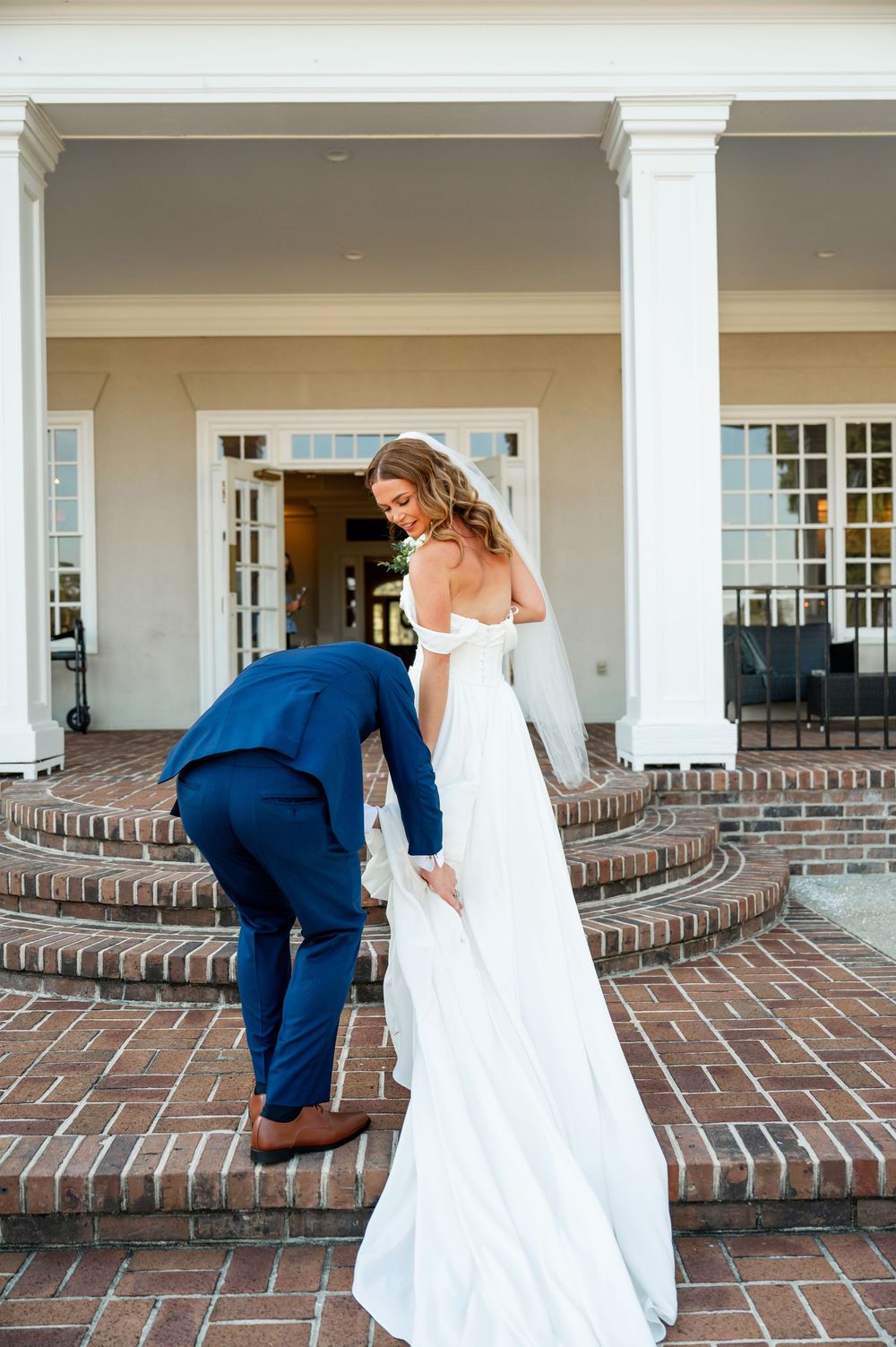 Bride and groom share a moment on brick porch with white columns.